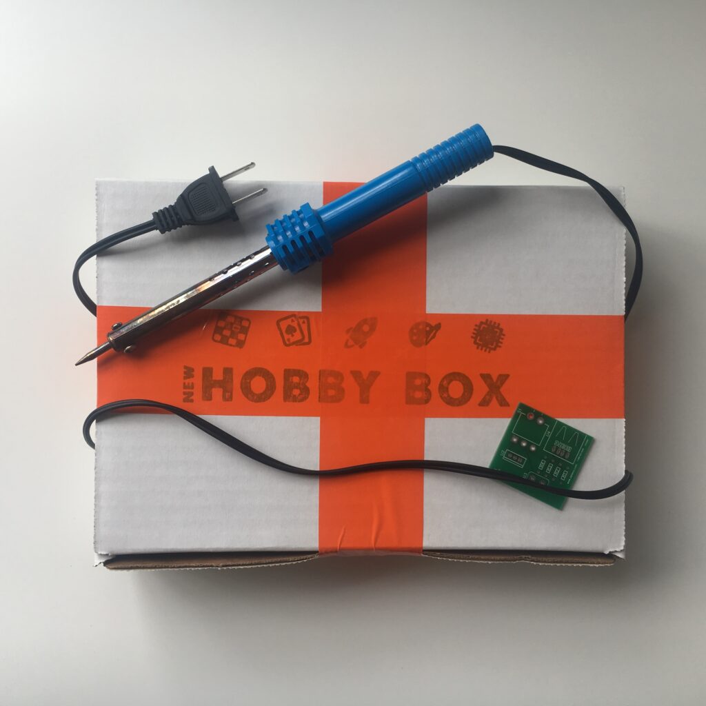 new hobby box electronics kit with soldering iron and computing chip lying on the front of a box