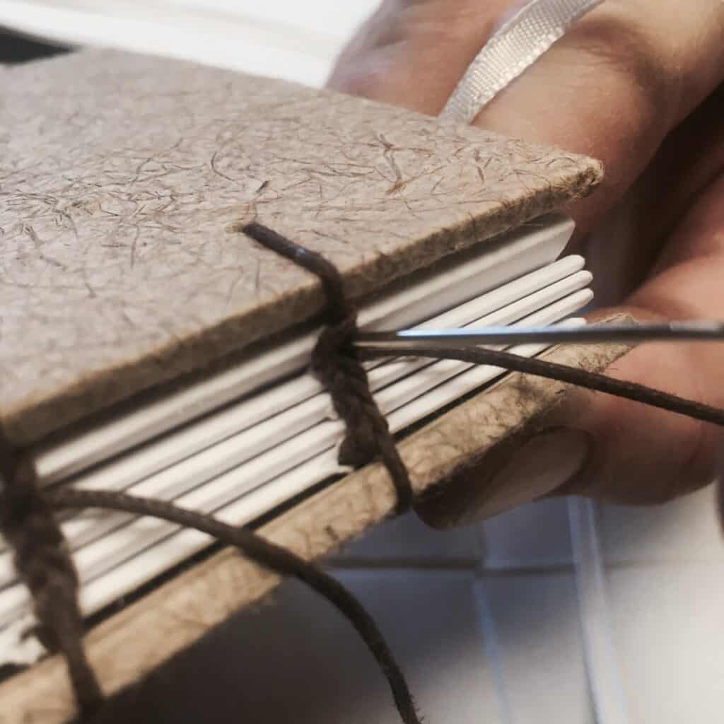 close up of threading a coptic stitch book