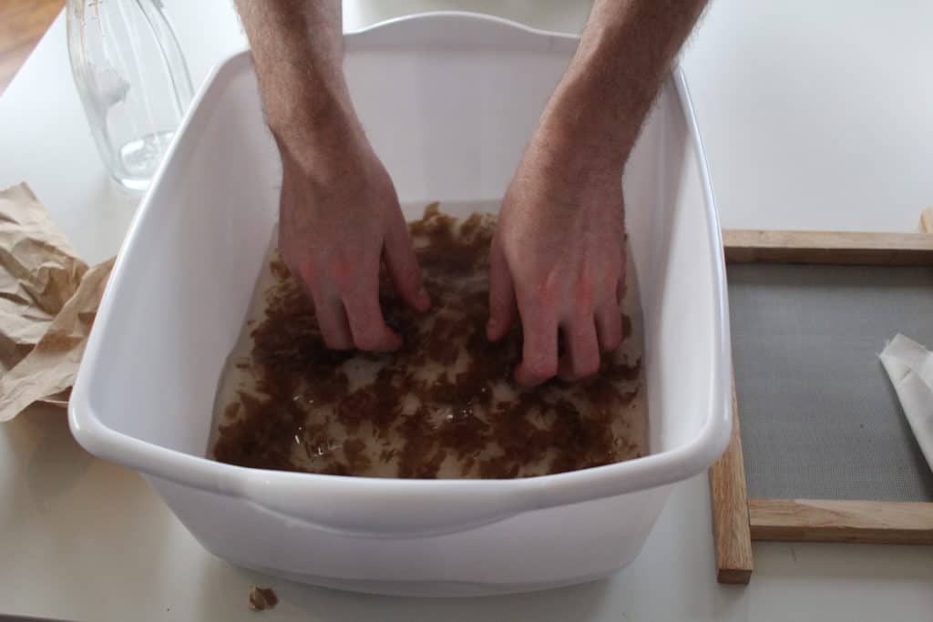 hands mixing shredded paper in tub of water